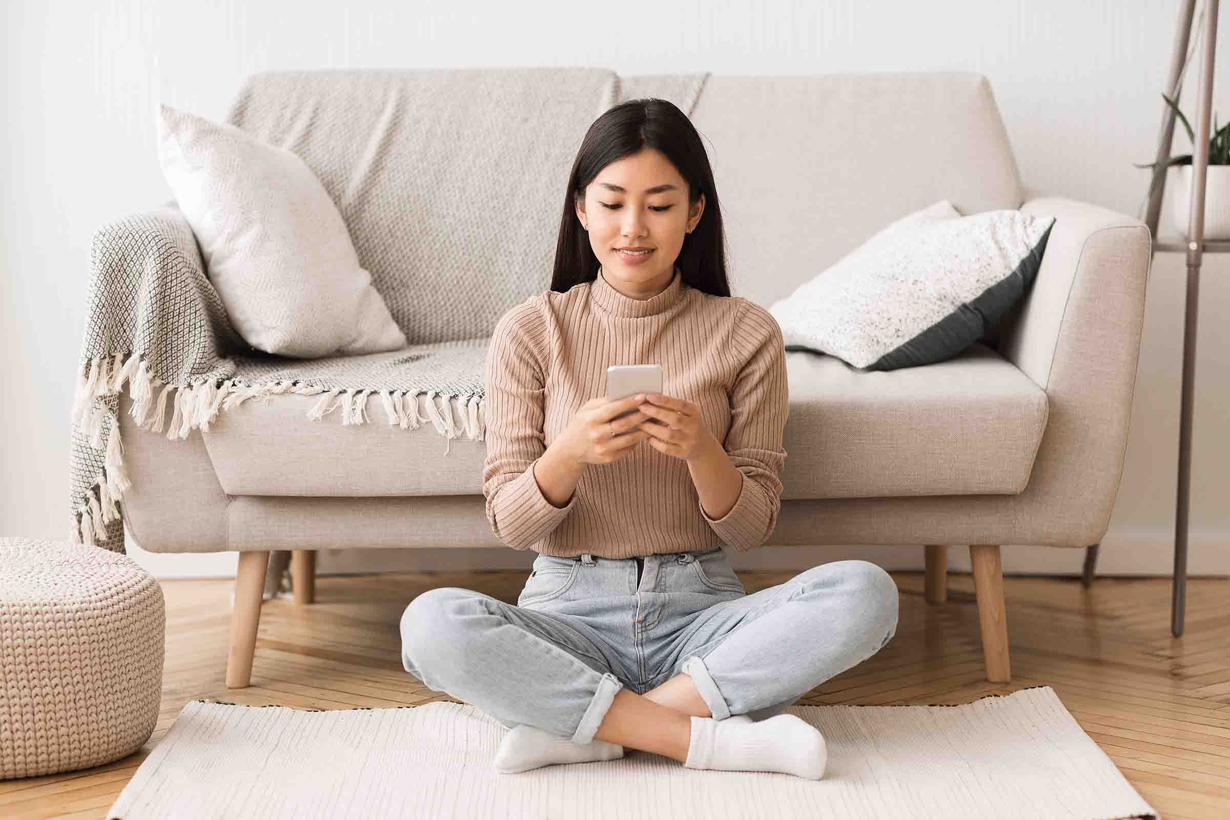Lady sitting on a warm floor using her phone.